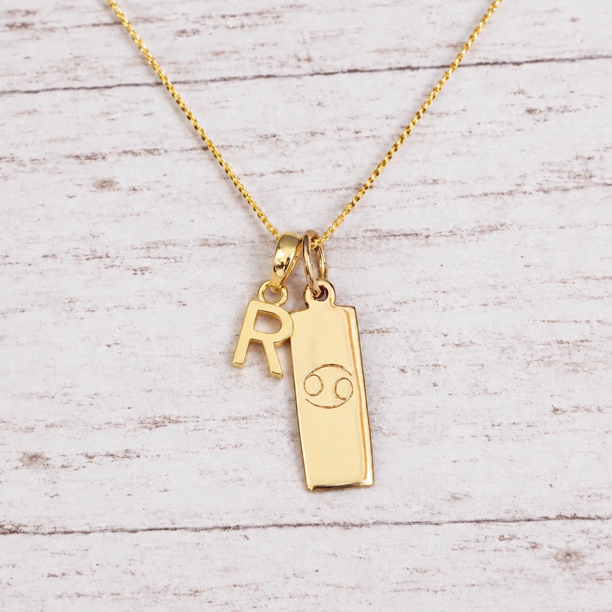 Gold Initial and Cancer Zodiac Necklace with letter R pendant on light wood