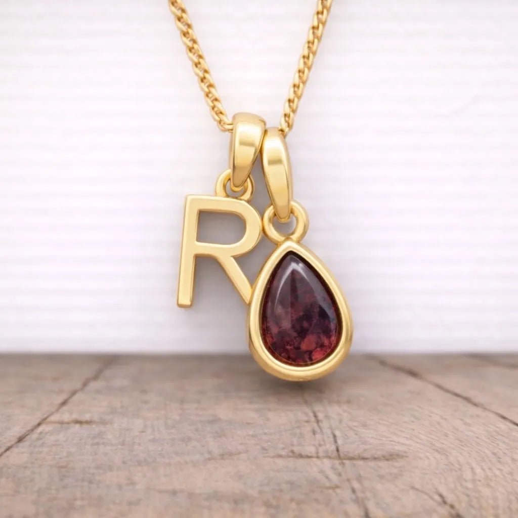 gold r initial and january birthstone garnet necklace hanging above a wooden surface