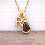 gold r initial and january birthstone garnet necklace hanging above a wooden surface