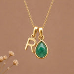 Gold Initial R and May Birthstone Emerald Necklace against a warm background