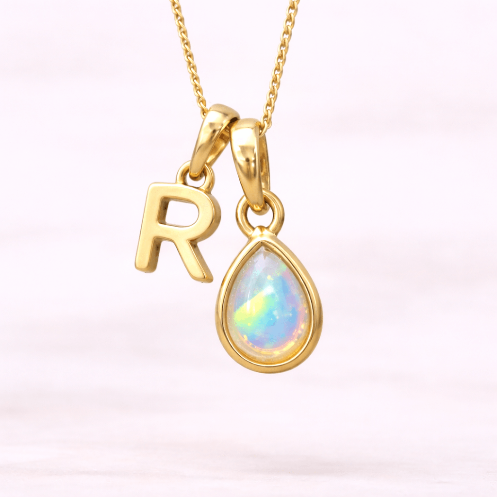 Gold necklace with 'R' pendant and teardrop-shaped opal on a light pink background