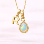 Gold October birthstone necklace with a pear-shaped natural opal pendant and letter 'R' charm with a light background.