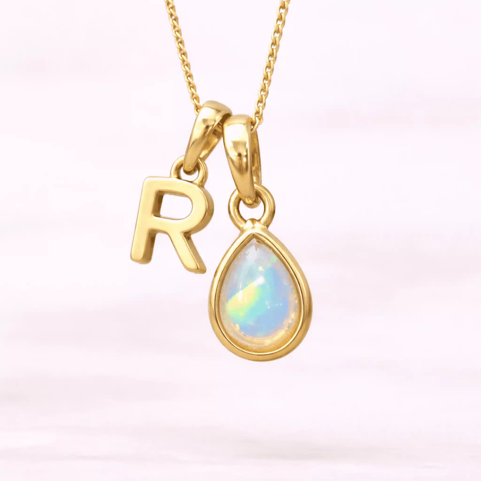 Gold October birthstone necklace with a pear-shaped natural opal pendant and letter 'R' charm with a light background.
