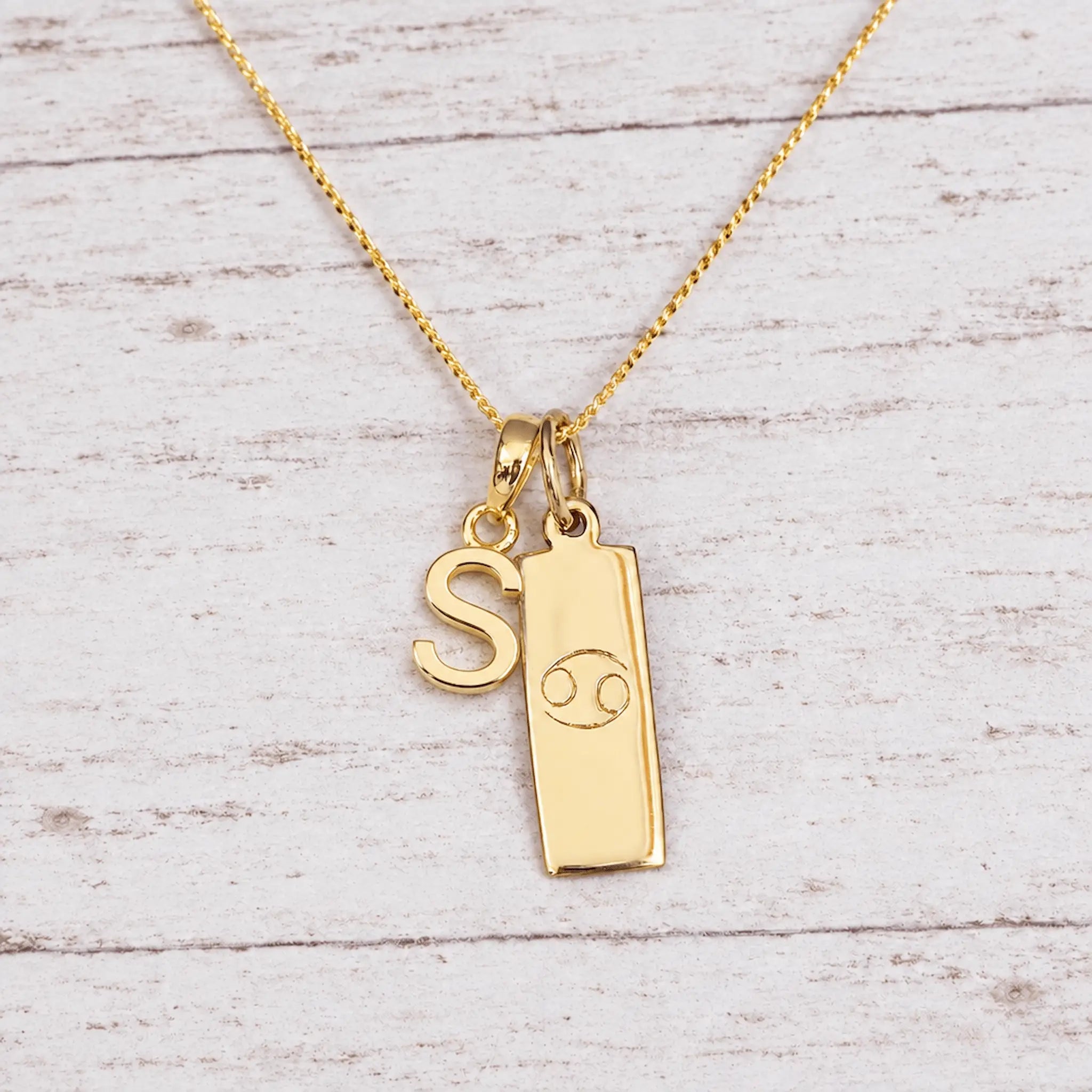 Gold Initial and Cancer Zodiac Necklace with letter S pendant on light wood