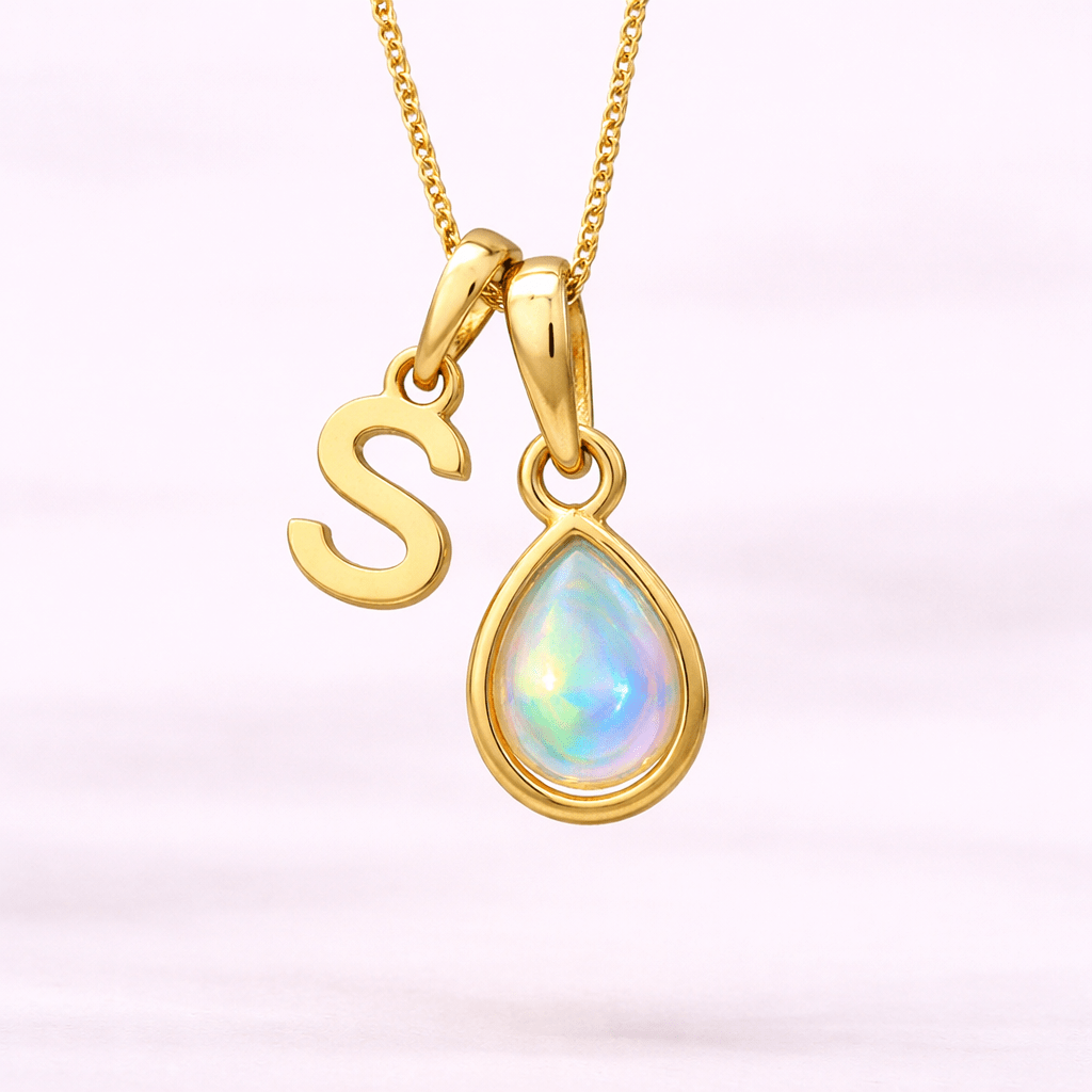 Gold necklace with 'S' pendant and teardrop-shaped opal gem on a light pink background