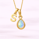 Gold necklace with 'S' pendant and teardrop-shaped opal gem on a light pink background