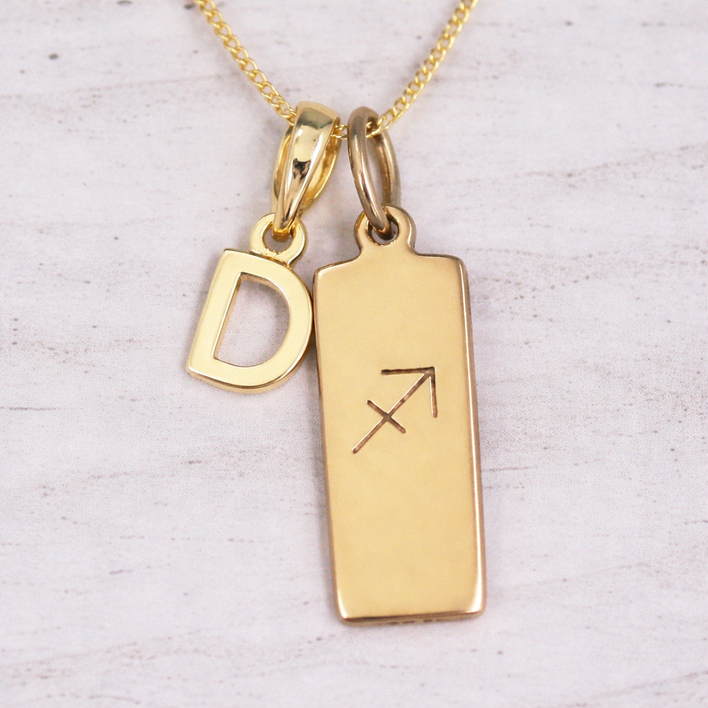 Gold necklace with 'D' pendant and Sagittarius symbol on a light background