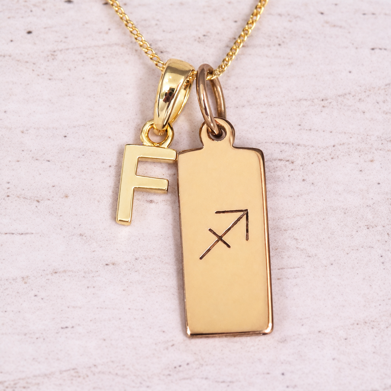 Gold necklace with 'F' pendant and Sagittarius symbol on a light background