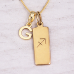 Gold necklace with 'G' pendant and rectangular tag with astrological symbol on a light background