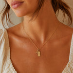 model wearing a gold double pendant necklace with an initial letter pendant and a rectangle pendant with sagittarius zodiac glyph