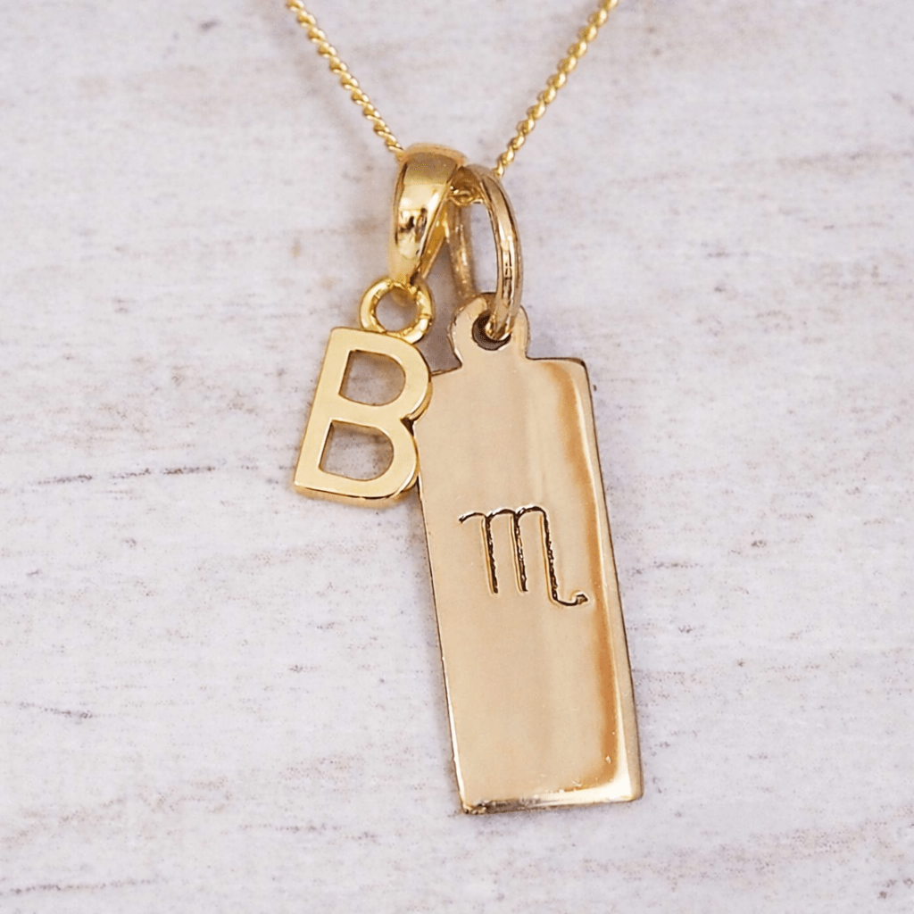 Gold necklace with 'B' pendant and Scorpio Zodiac pendants on a light gray background