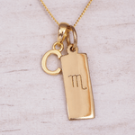 Gold necklace with 'C' initial and scorpio zodiac symbol on a light wooden background