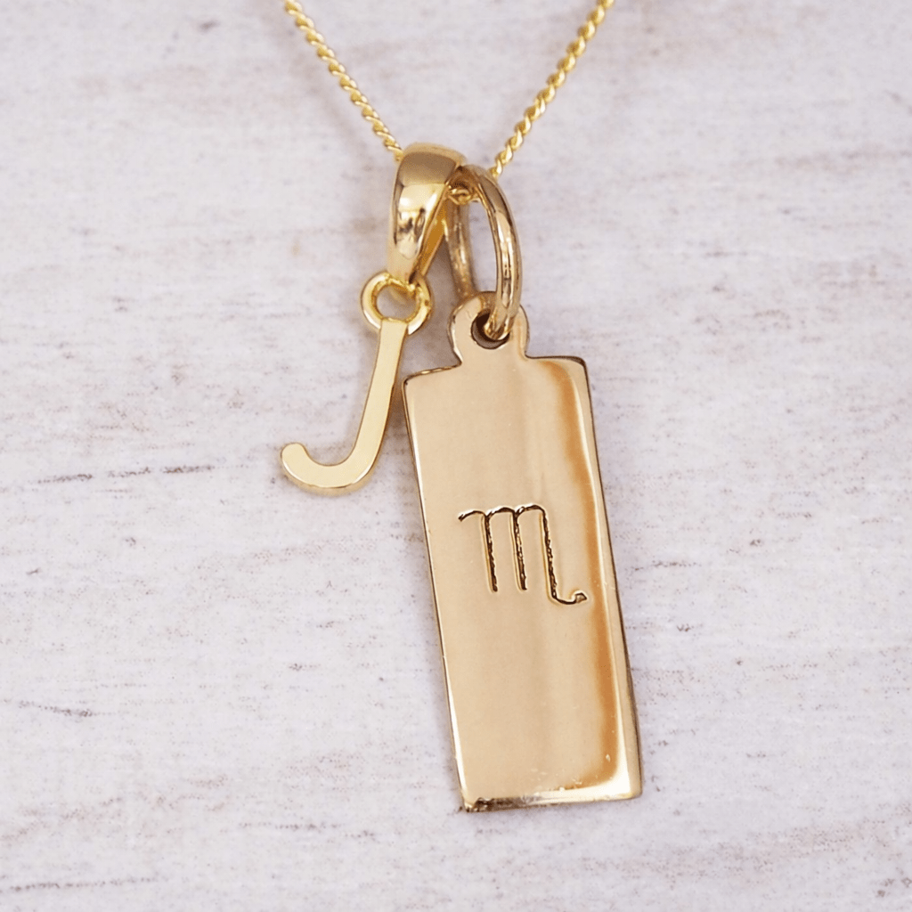 Gold necklace with a 'J' initial pendant and a Scorpio zodiac symbol on a light gray background