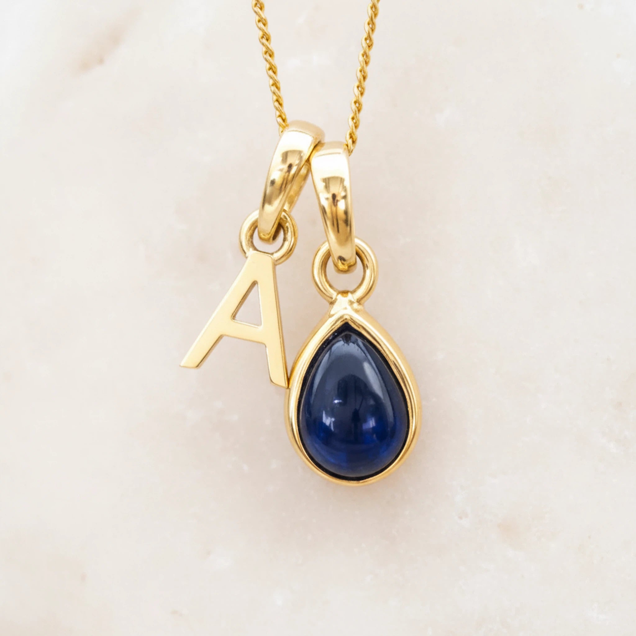 Gold September birthstone necklace with a blue sapphire teardrop pendant and letter 'A' charm