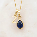 Gold Z initial pendant necklace with a pear shaped september birthstone sapphire gemstone on a light background.