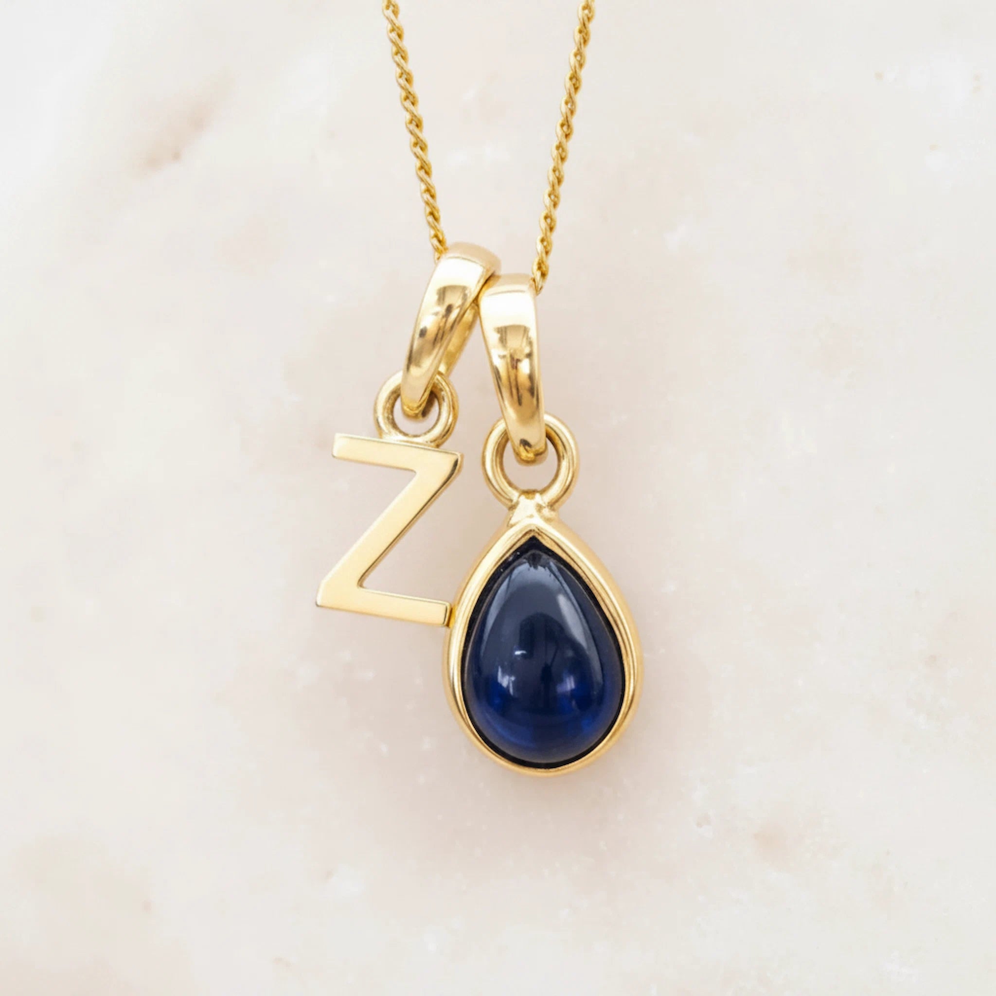 Gold Z initial pendant necklace with a pear shaped september birthstone sapphire gemstone on a light background.