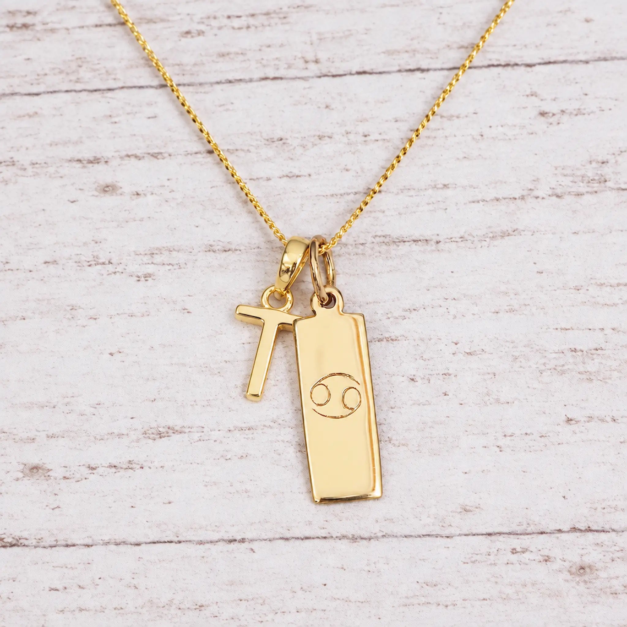 Gold Initial and Cancer Zodiac Necklace with letter T pendant on light wood
