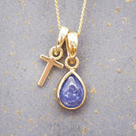 Gold December birthstone necklace with a pear-shaped natural tanzanite pendant and letter 'T' charm with a grey background.