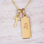 Gold initial and Leo zodiac necklace with a letter T pendant and engraved Leo bar on white wood, close-up