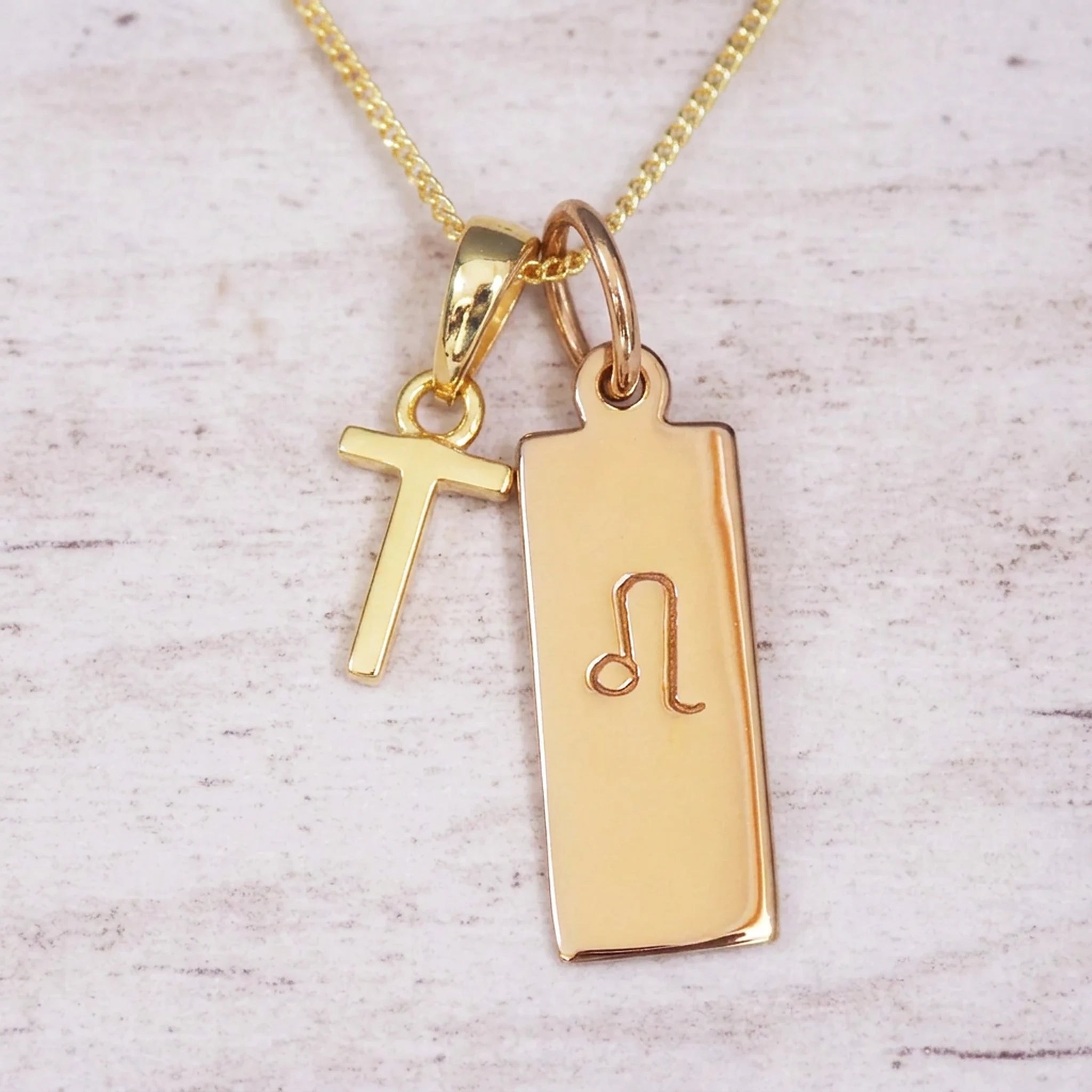 Gold initial and Leo zodiac necklace with a letter T pendant and engraved Leo bar on white wood, close-up