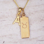 Gold necklace with 'A' initial pendant and Taurus zodiac Star sign symbol pendant on a light wooden background