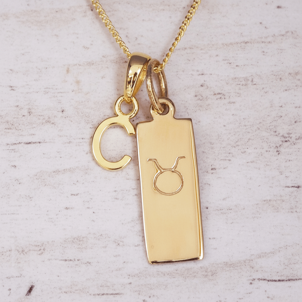 Gold necklace with a Taurus zodiac symbol pendant and 'C' initial on a light wooden background
