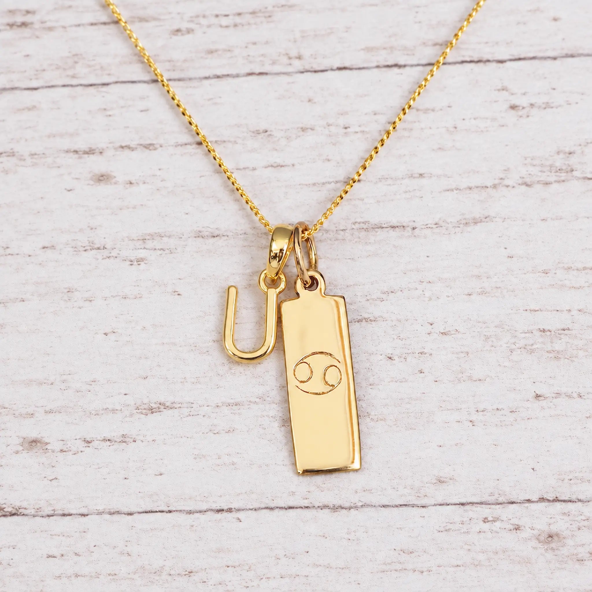 Gold Initial and Cancer Zodiac Necklace with letter U pendant on light wood