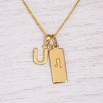 Gold initial and Leo zodiac necklace with a letter U pendant and engraved Leo bar on white wood, close-up