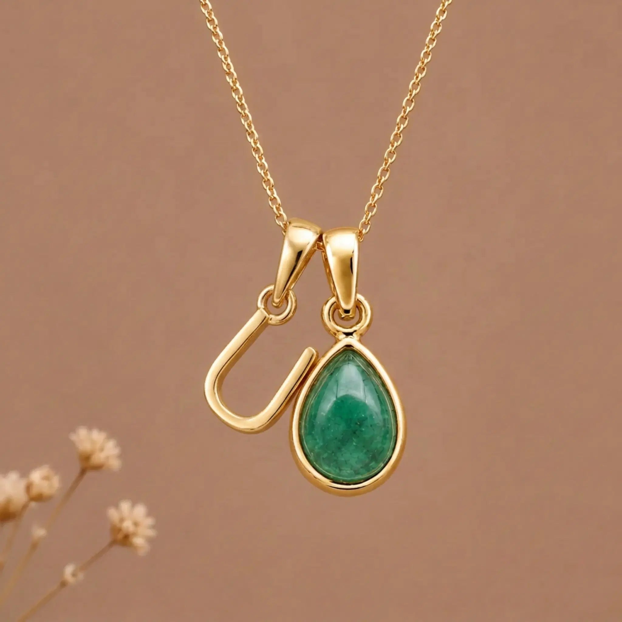 Gold Initial U and May Birthstone Emerald Necklace against a warm background