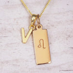 Gold initial and Leo zodiac necklace with a letter V pendant and engraved Leo bar on white wood, close-up