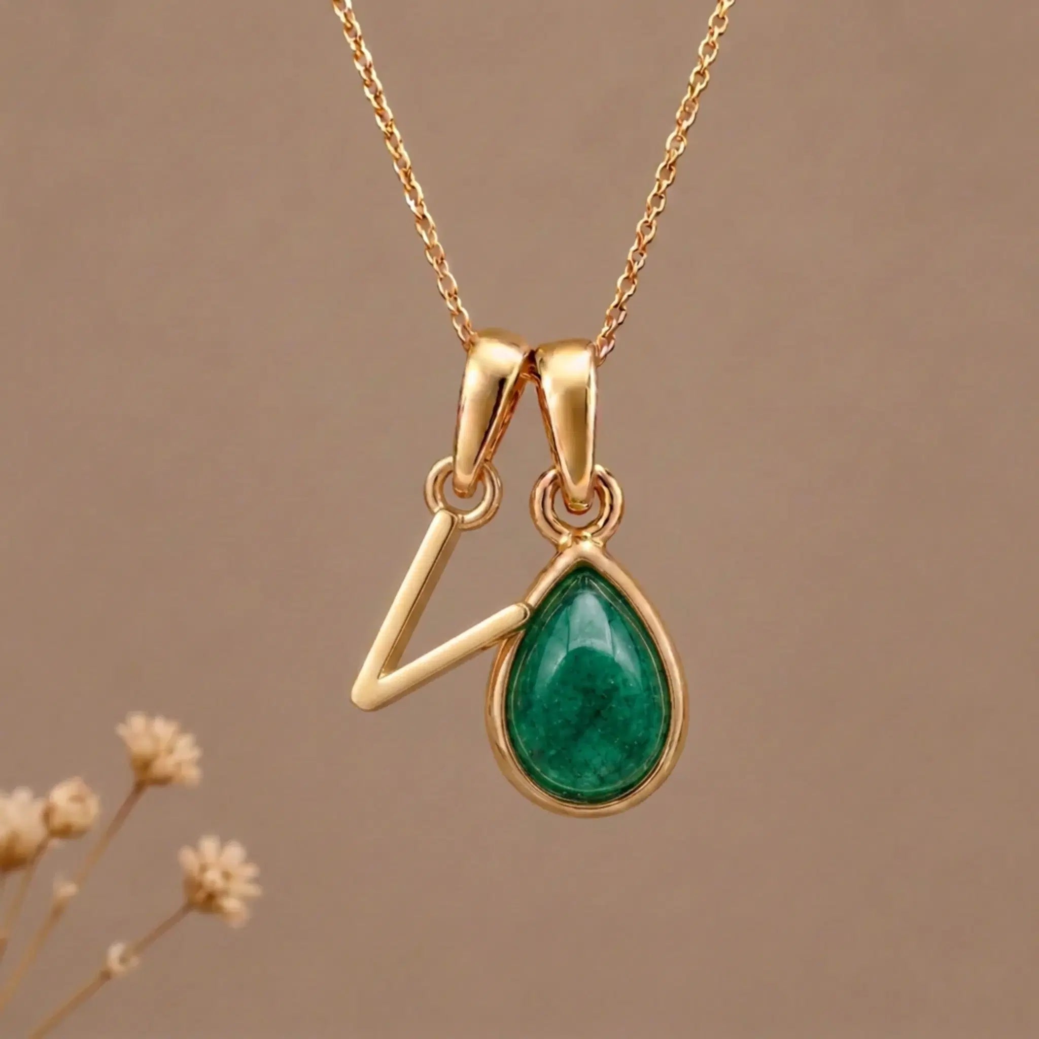Gold Initial v and May Birthstone Emerald Necklace against a warm background
