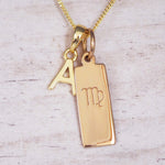 Gold necklace with a pendant featuring the letter 'A' and a virgo zodiac symbol pendant on a light wooden background.