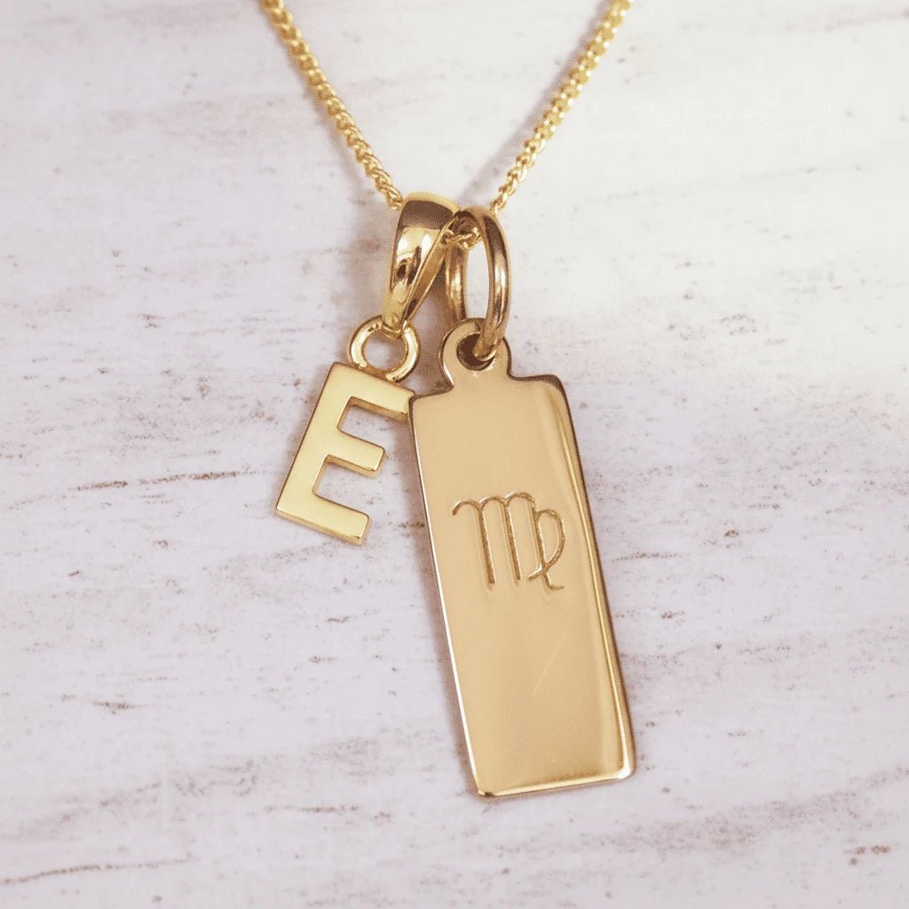 Gold necklace with 'E' initial pendant and Virgo zodiac sign on a light wooden background