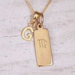 Gold necklace with 'G' initial pendant and Virgo zodiac sign on a light wooden background