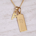 Gold necklace with 'P' initial pendant and Virgo zodiac sign on a light wooden background