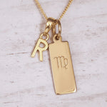 Gold necklace with 'R' initial pendant and Virgo zodiac sign on a light wooden background