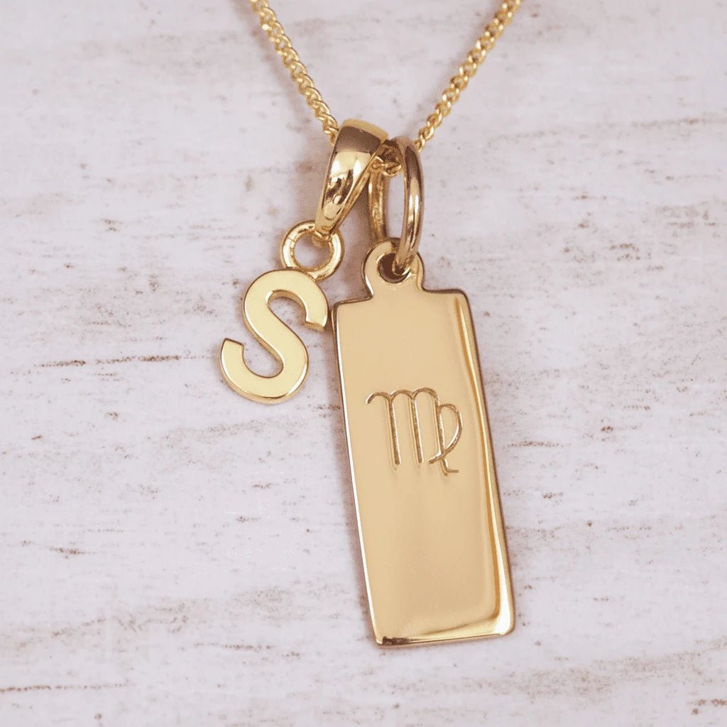 Gold necklace with 'S' initial pendant and Virgo zodiac sign on a light wooden background