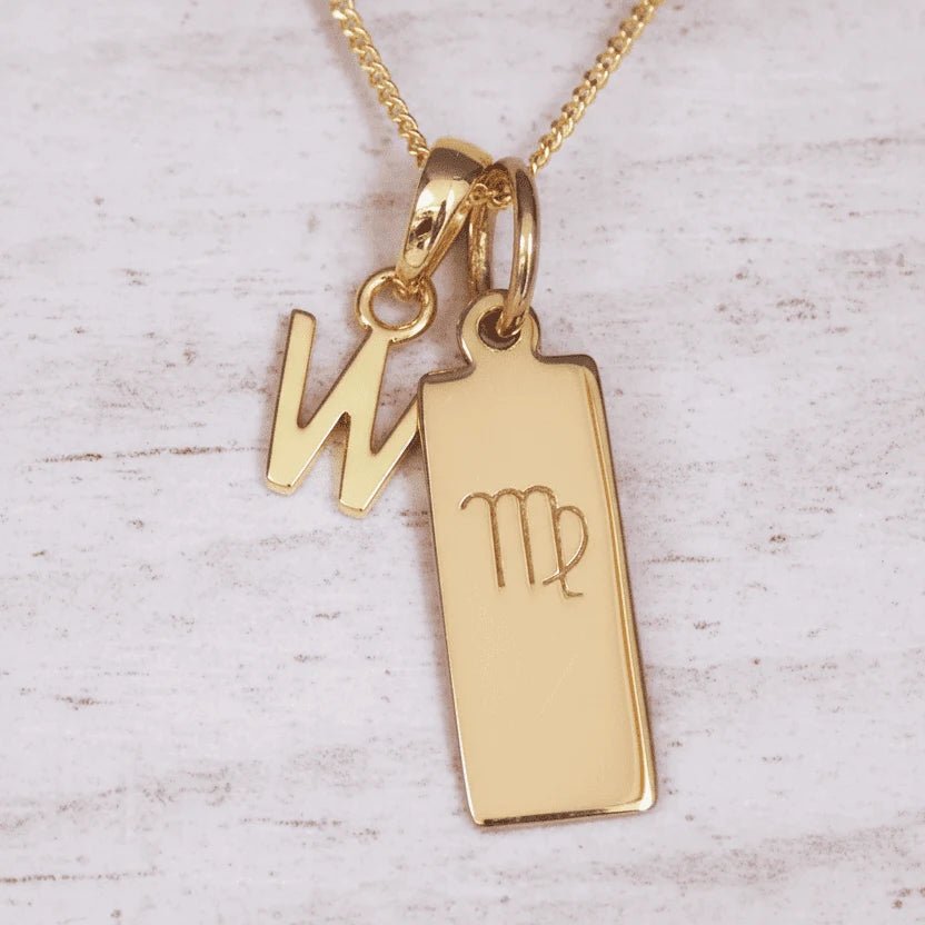 Gold necklace with 'W' initial pendant and Virgo zodiac sign on a light wooden background