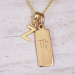 Gold double pendant necklace with a rectangular pendant with virgo zodiac glyph and a letter Z pendant on a light wooden background