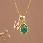 Gold Initial W and May Birthstone Emerald Necklace against a warm background