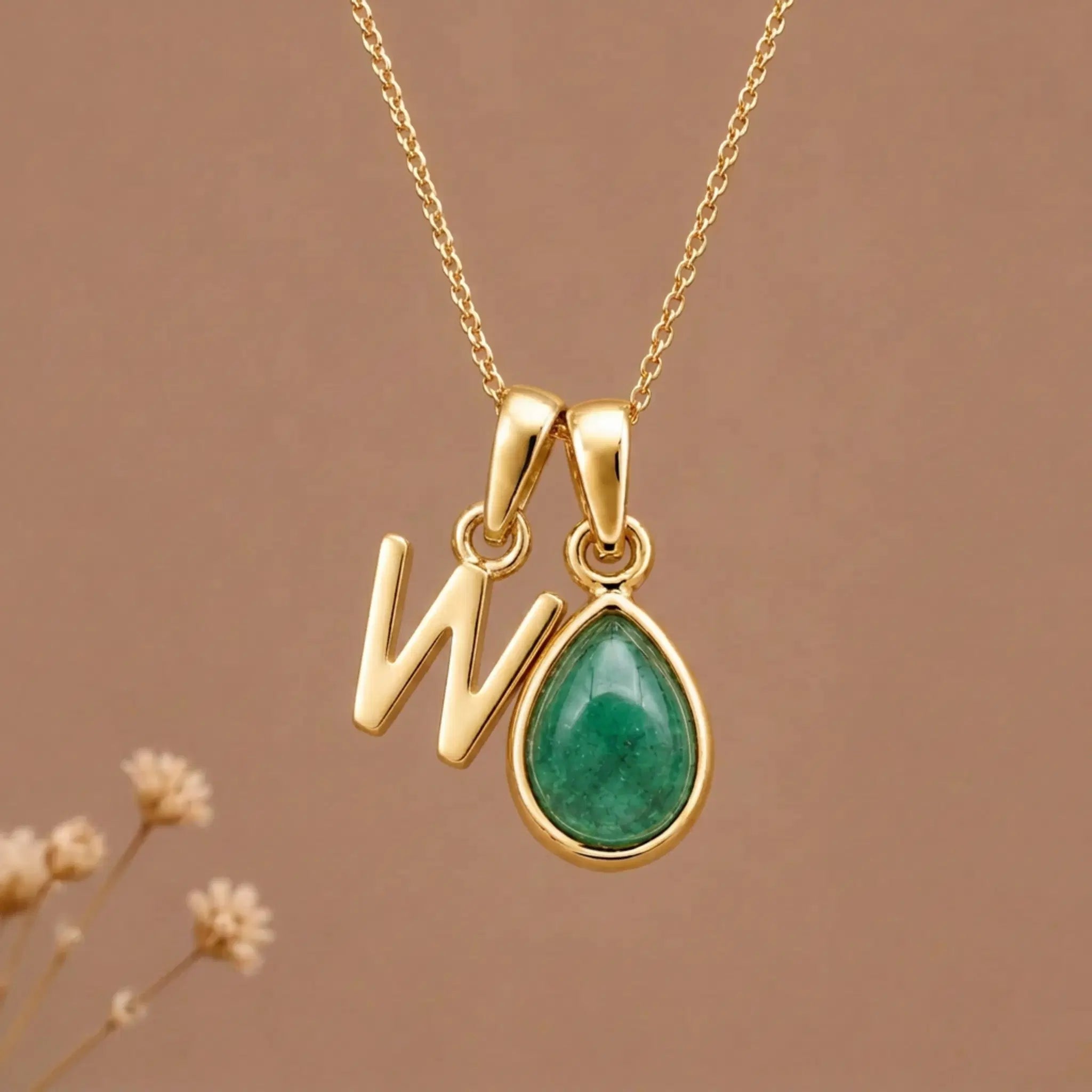 Gold Initial W and May Birthstone Emerald Necklace against a warm background
