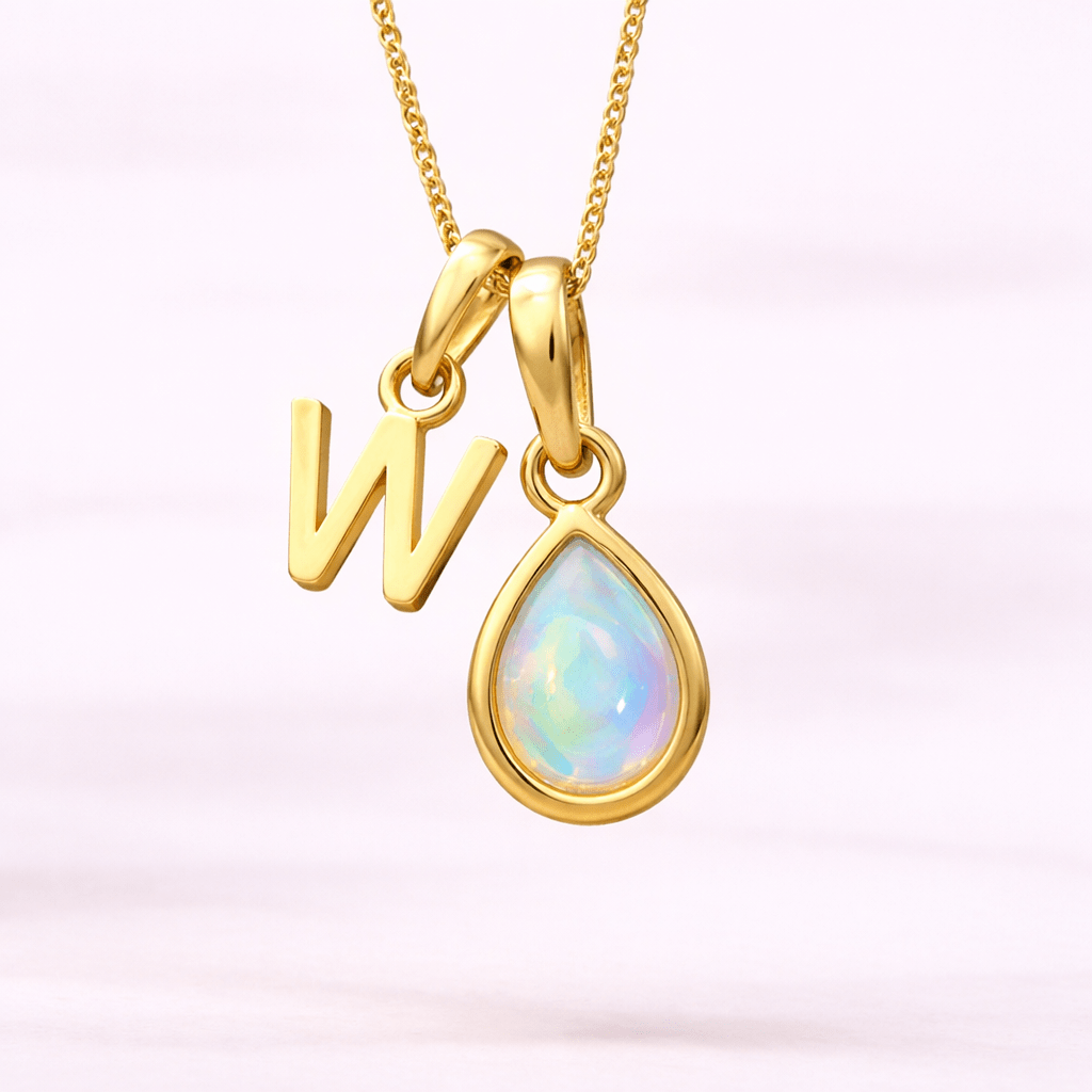 Gold necklace with 'W' pendant and teardrop-shaped opal on a light pink background