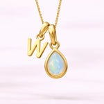 Gold October birthstone necklace with a pear-shaped natural opal pendant and letter 'W' charm with a light background.