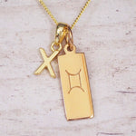 Gold initial X and Gemini zodiac bar necklace, close-up of the letter charm and engraved pendant on whitewashed wood