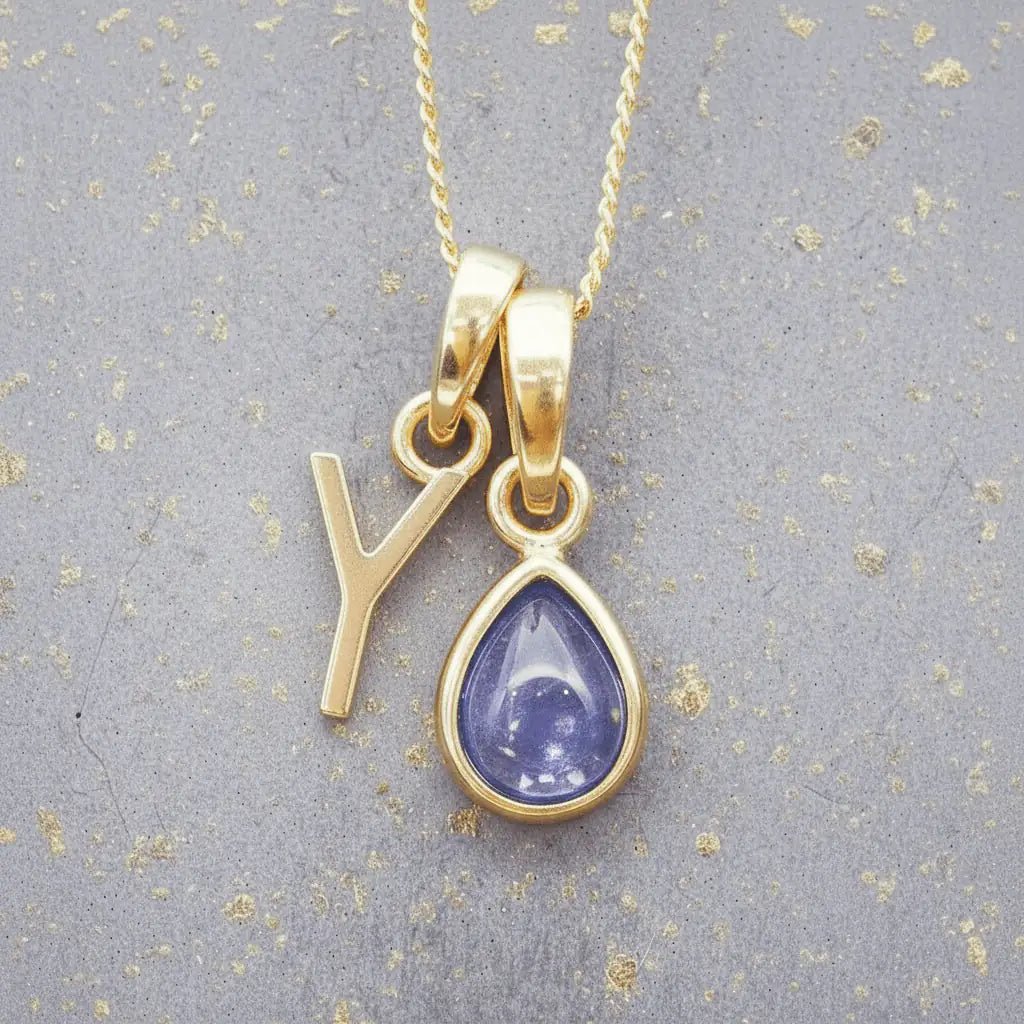 Gold December birthstone necklace with a pear-shaped natural tanzanite pendant and letter 'Y' charm with a grey background.