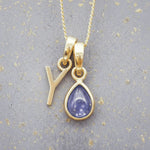 Gold December birthstone necklace with a pear-shaped natural tanzanite pendant and letter 'Y' charm with a grey background.