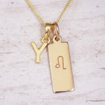 Gold initial and Leo zodiac necklace with a letter Y pendant and engraved Leo bar on white wood, close-up