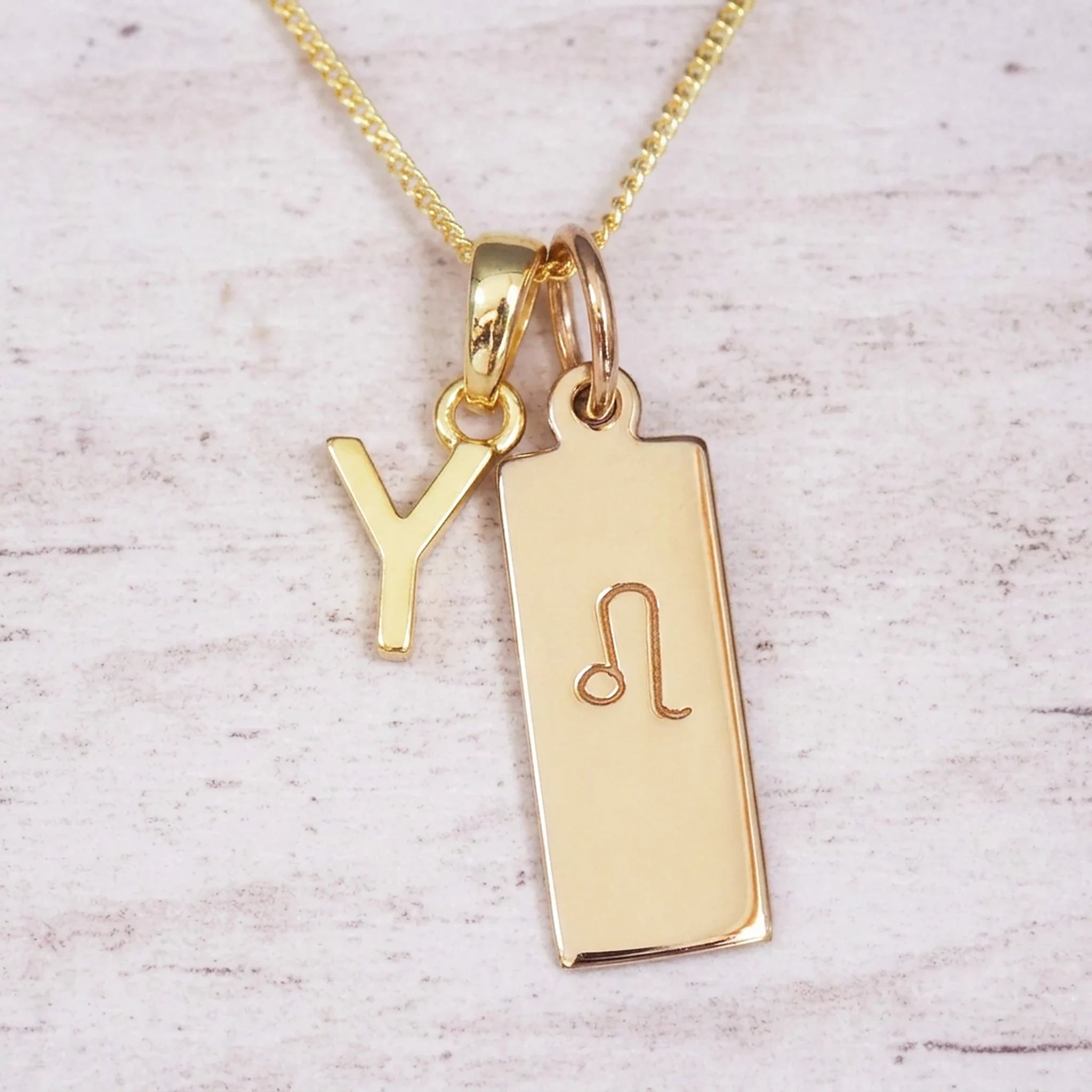 Gold initial and Leo zodiac necklace with a letter Y pendant and engraved Leo bar on white wood, close-up