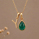 Gold Initial Y and May Birthstone Emerald Necklace against a warm background