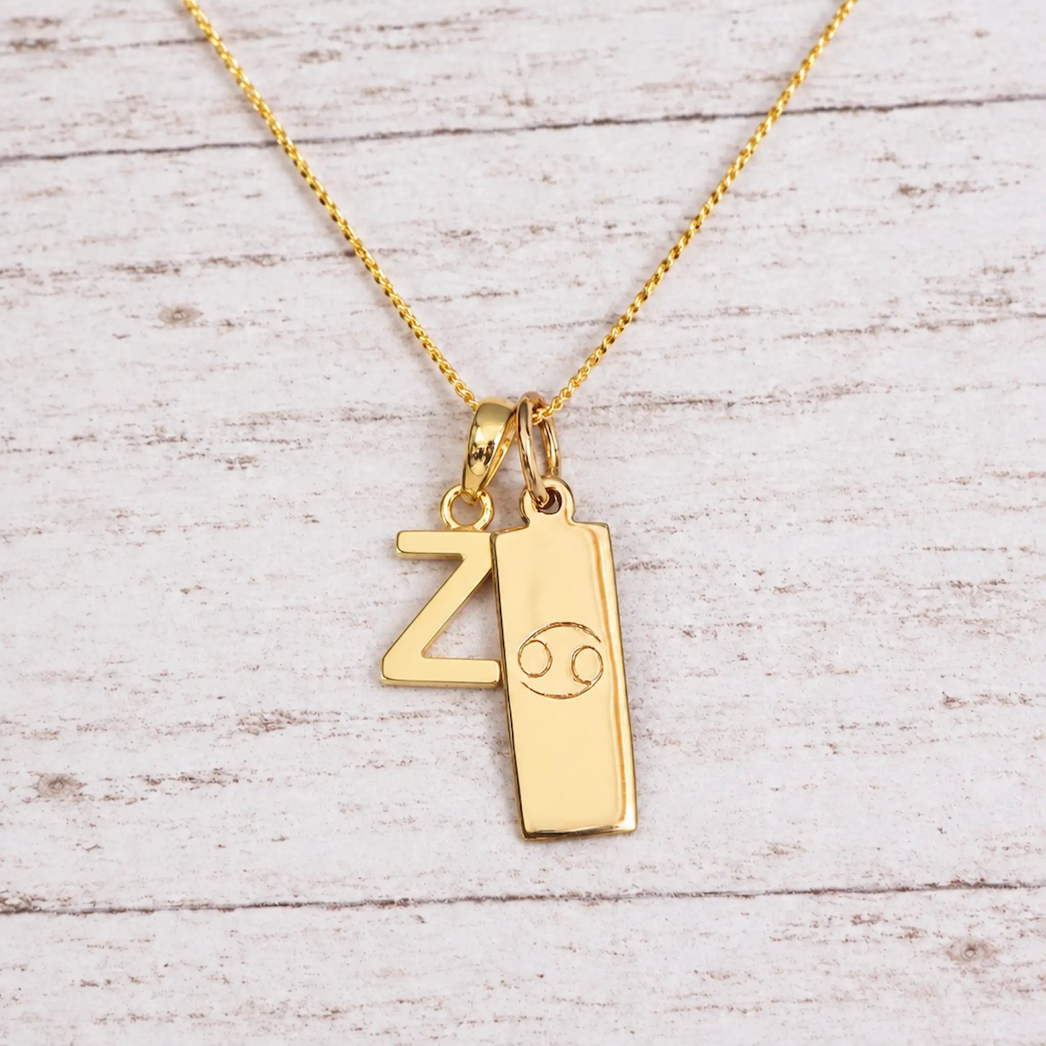 Gold Initial and Cancer Zodiac Necklace with letter Z pendant on light wood